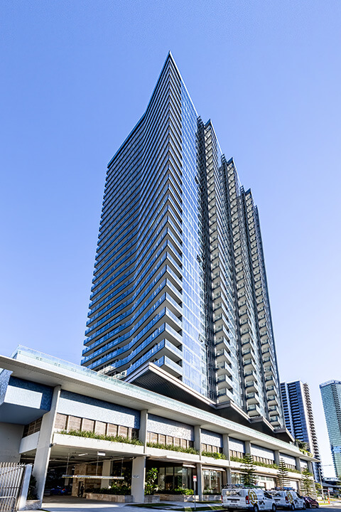 Exterior view of ULTIQA Signature at Broadbeach, a modern high-rise building with sleek glass architecture against a clear blue sky.
