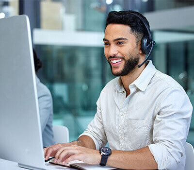 Smiling customer service representative wearing a headset, working at a computer in a modern office.