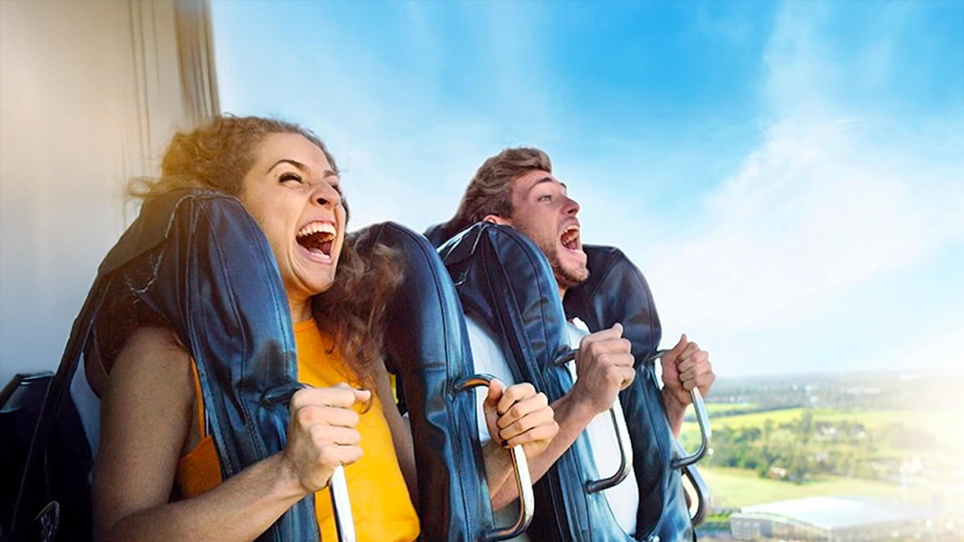 Two people screaming with excitement on a thrill ride with scenic views in the background.