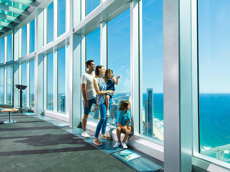 Family enjoying panoramic views of the coastline and city from a high-rise observation deck.