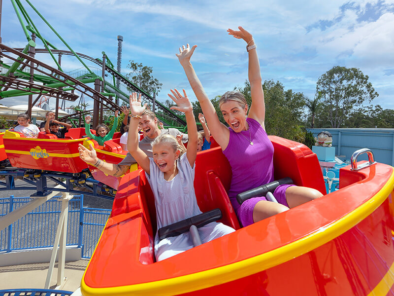 Family enjoying a colourful roller coaster ride with hands in the air at a theme park.