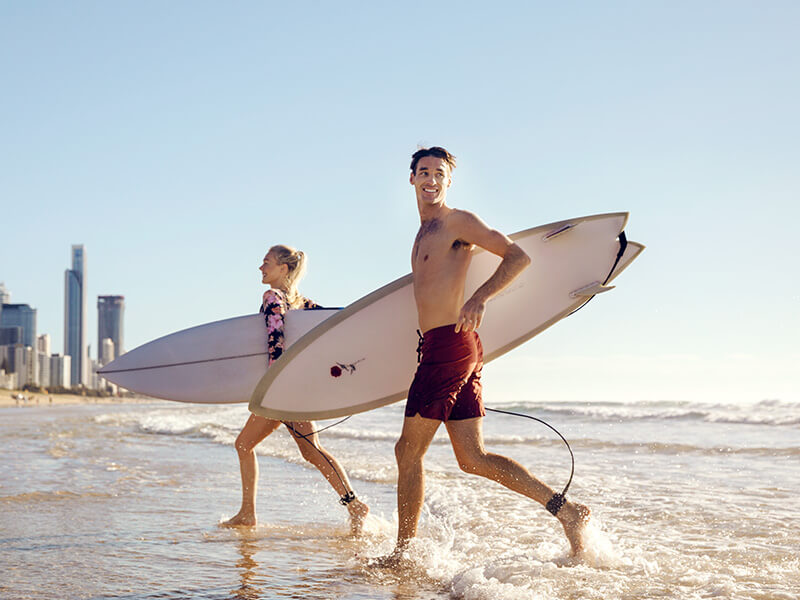 Couple walking from the ocean with surfboards along a Gold Coast beach.