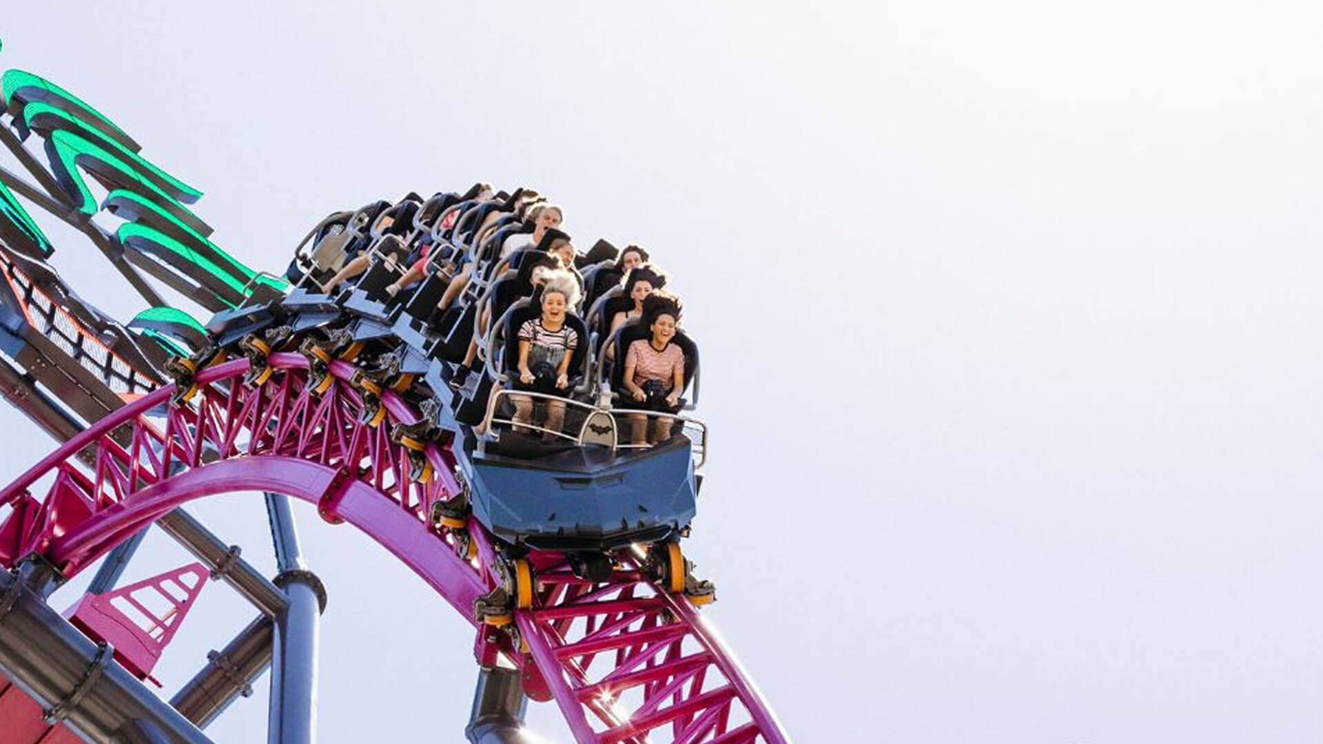 Thrill-seekers riding a high-speed roller coaster with steep loops and vibrant pink and green tracks.