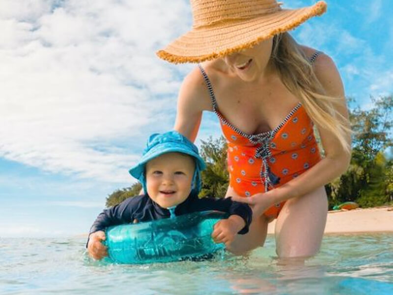 Smiling mother in a sunhat and baby in a bucket hat enjoying a sunny day in shallow water.