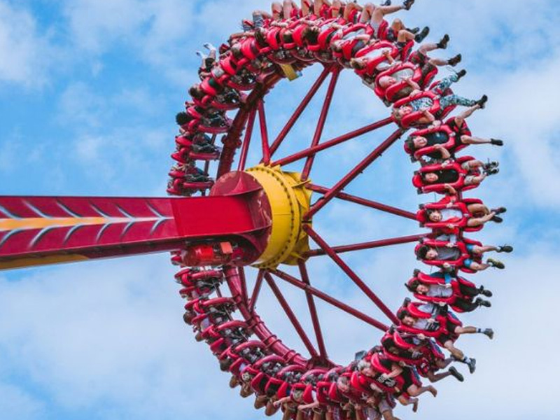 People riding a giant spinning pendulum thrill ride against a blue sky, experiencing high-speed excitement.