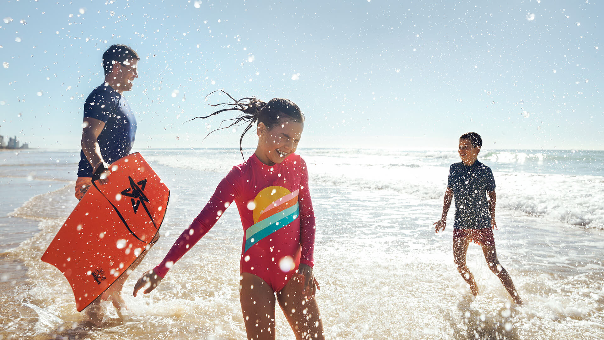 Family playing in the waves on the Gold Coast, enjoying a Broadbeach beach holiday.