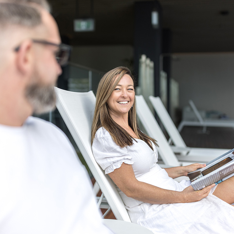Couple relaxing on loungers at a Gold Coast resort, with the woman smiling and reading a magazine