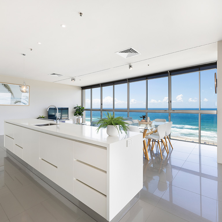 Oceanfront apartment at ULTIQA Air on Broadbeach featuring a modern open-plan kitchen, dining area, and floor-to-ceiling windows with panoramic beach views