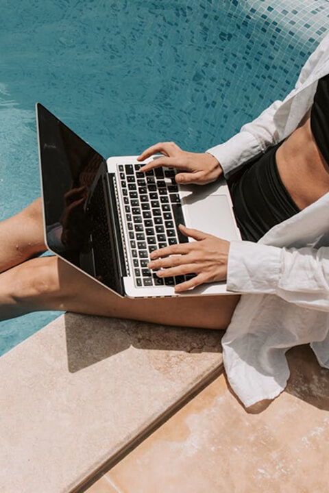 Person sitting by the pool working on a laptop, showcasing poolside relaxation with free WiFi and connectivity.