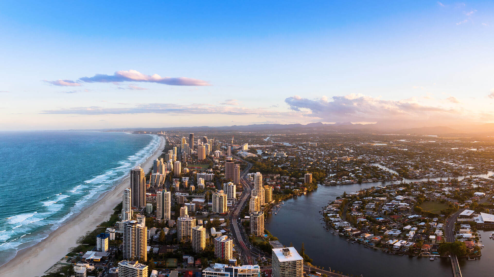 Aerial view of Gold Coast skyline, beachfront, and waterways at sunset.