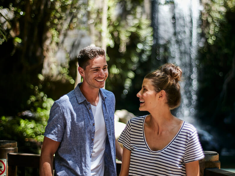 Smiling couple enjoying an outdoor nature experience with greenery and waterfall in the background.