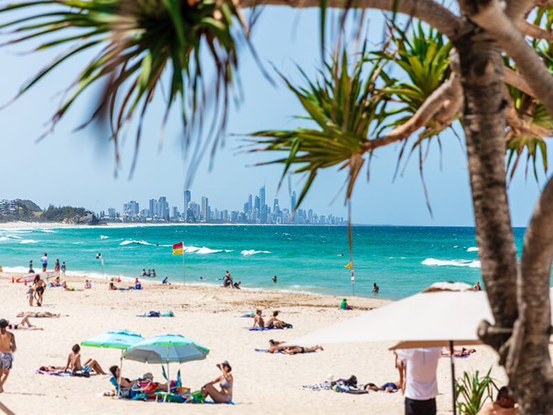 People relaxing on Burleigh Heads Beach with views of the Gold Coast skyline in the distance.