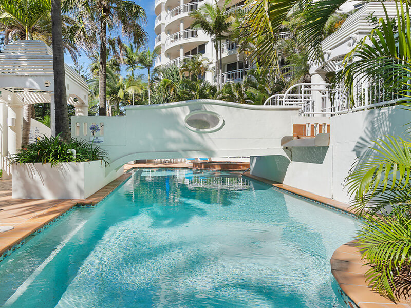 Outdoor resort pool surrounded by palm trees and tropical landscaping at ULTIQA Burleigh Mediterranean Resort.