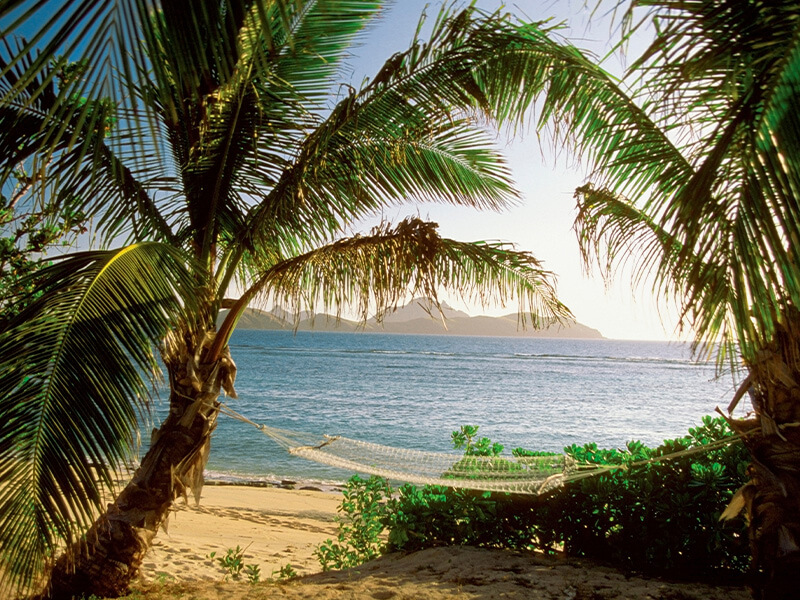 Hammock strung between palm trees on a tropical Fiji beach.
