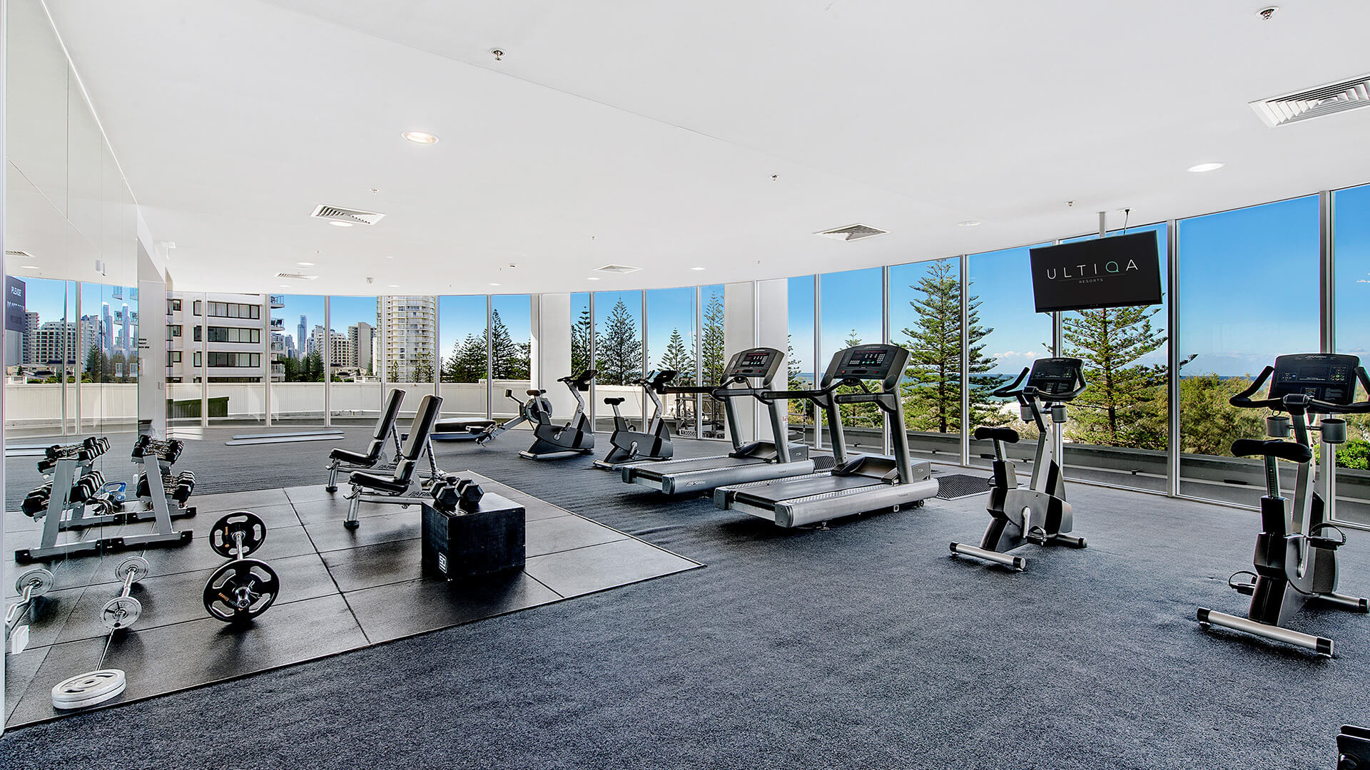 Fitness centre at ULTIQA Air on Broadbeach featuring cardio and weight equipment, large windows, and city views.