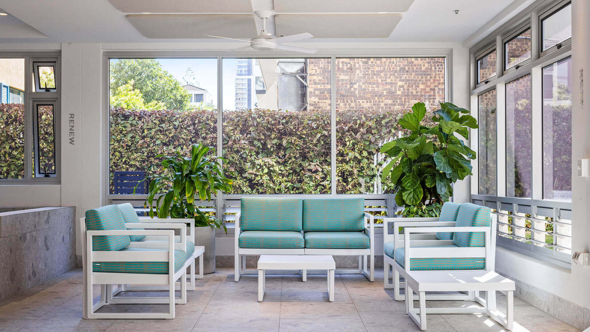 Indoor relaxation lounge at ULTIQA Beach Haven featuring modern coastal seating, lush indoor plants, and natural light - perfect for unwinding poolside.