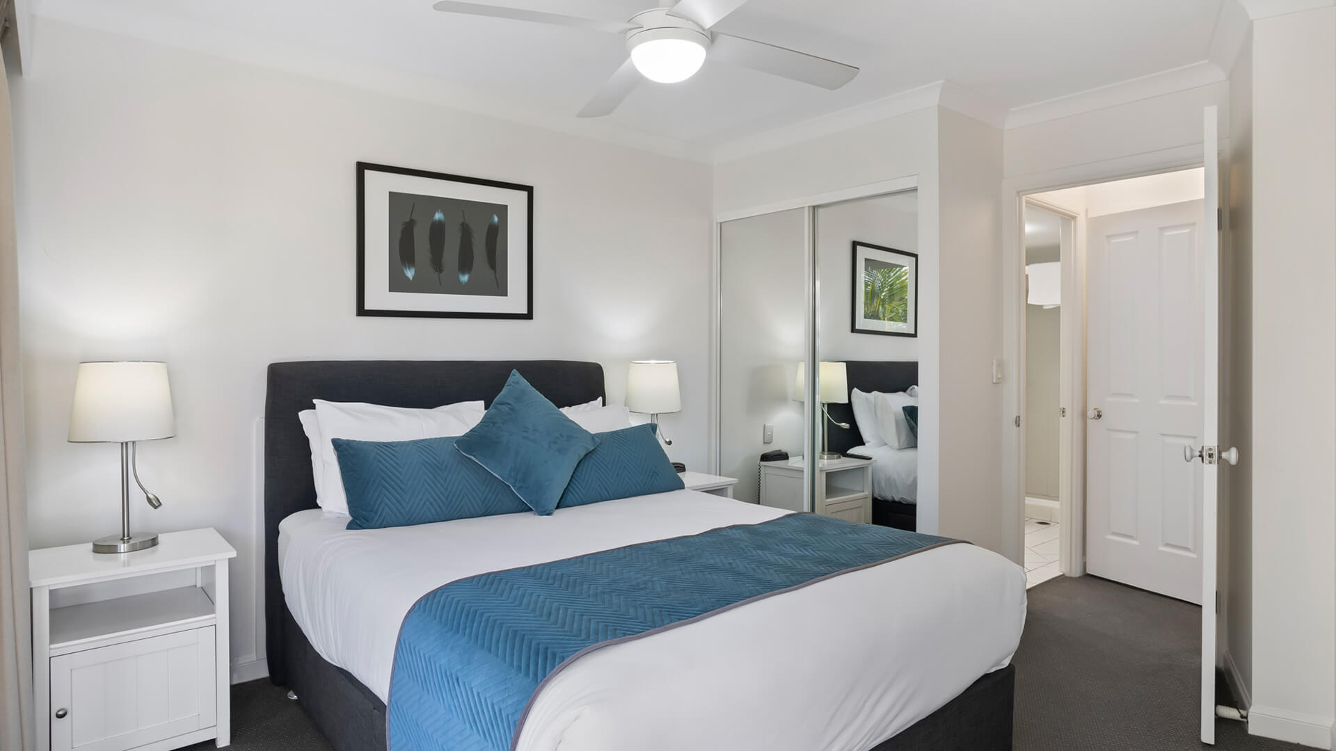 Bedroom with queen bed, mirrored wardrobe, and ceiling fan.