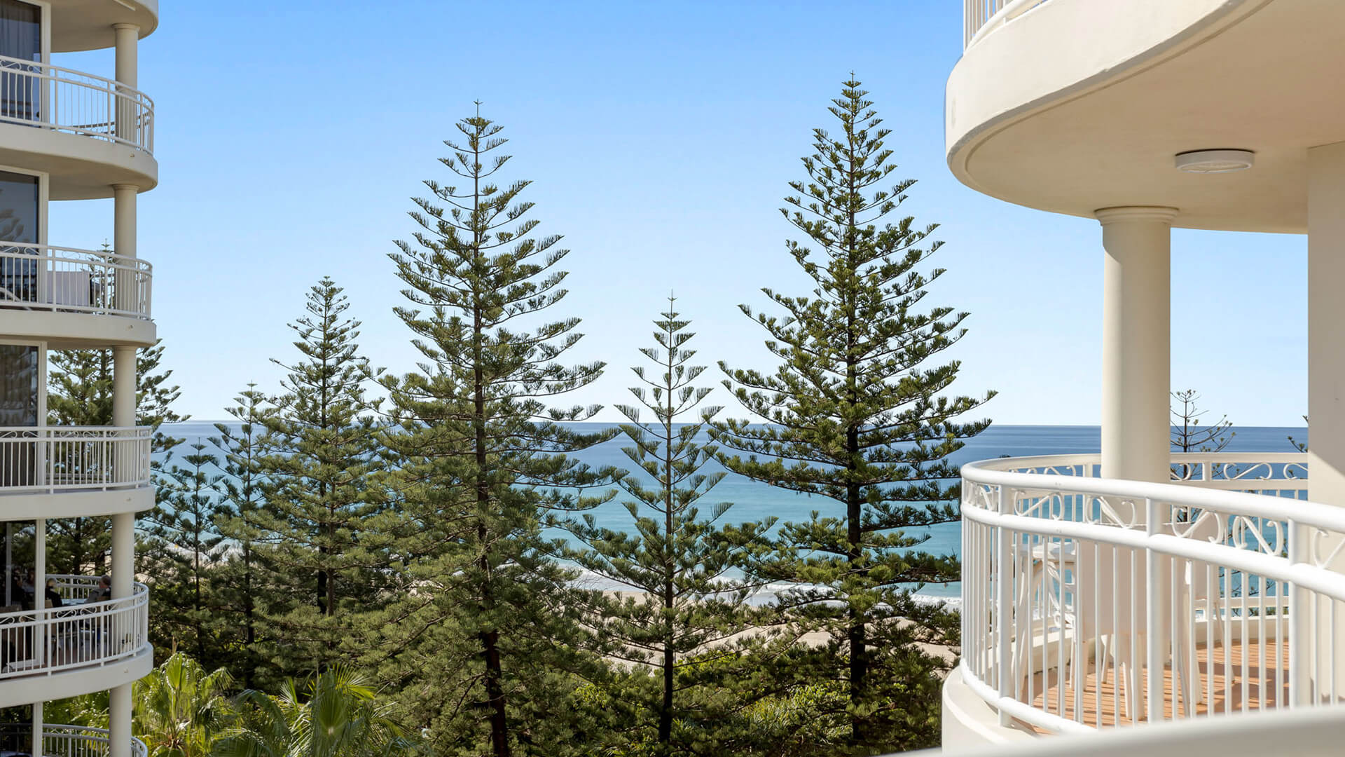 Ocean view from the balcony, framed by lush pines and curved railings.