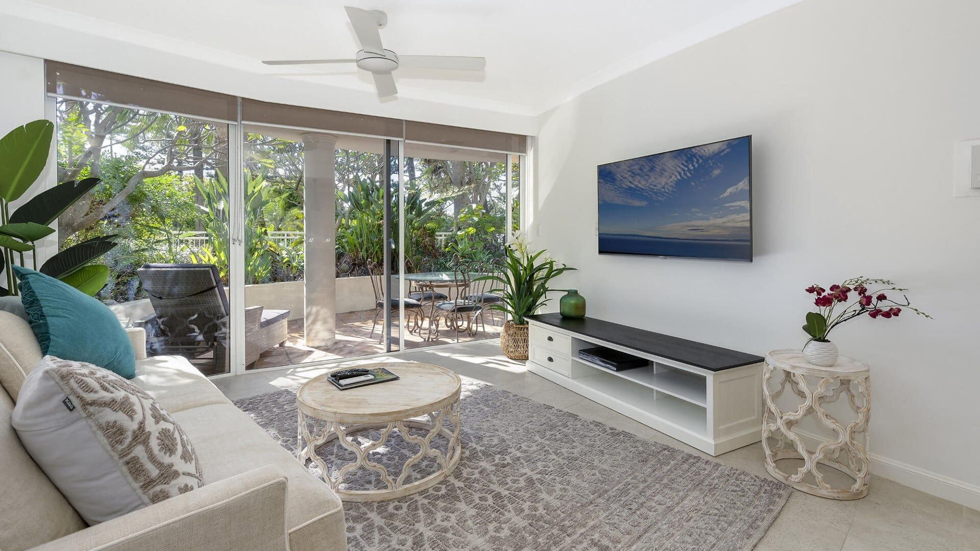 Living area in 1 Bedroom Superior Apartment at ULTIQA Burleigh Mediterranean Resort with smart TV and leafy patio access.