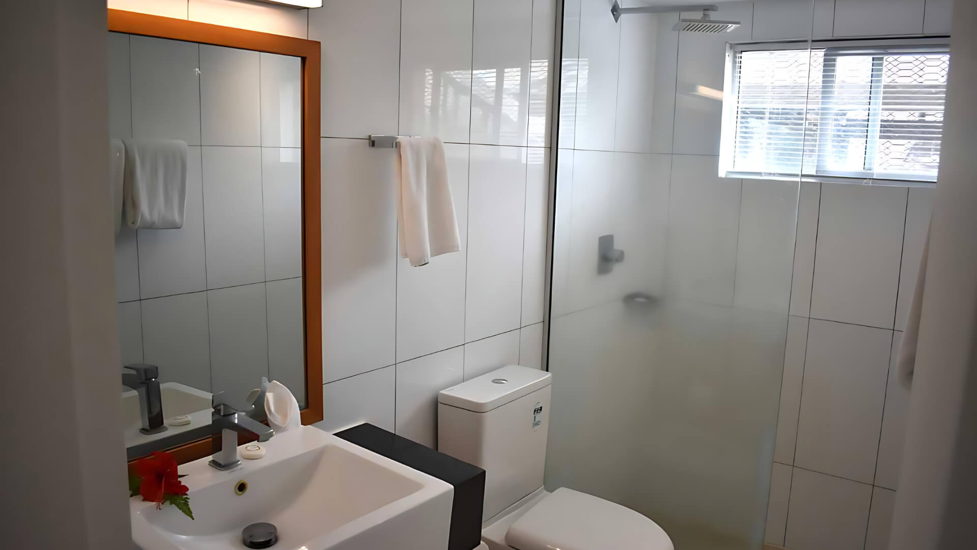 Bathroom in Standard 2 Bedroom 1 Bathroom Apartment at ULTIQA Fiji, featuring a glass-enclosed shower, toilet, vanity with mirror, and fresh towels.
