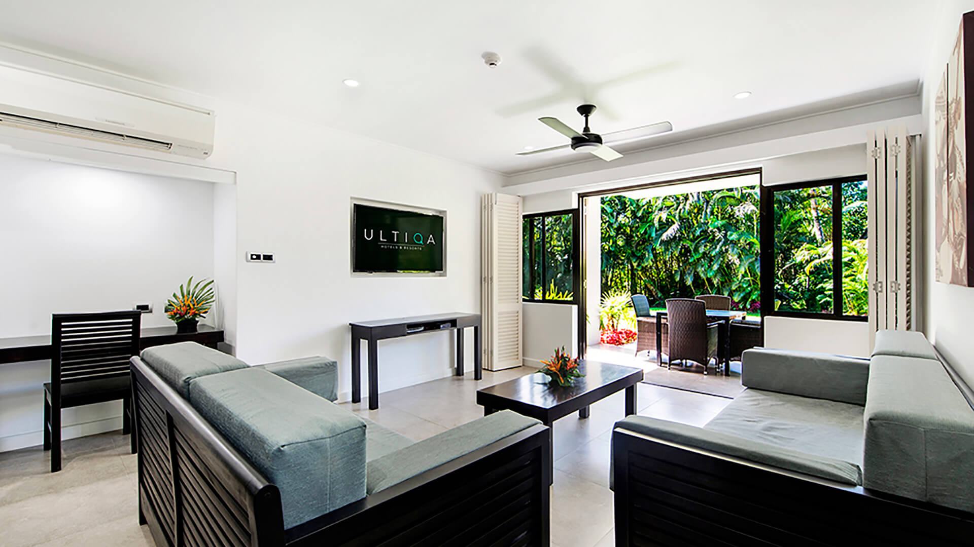 Spacious living area in 2 Bedroom Apartment at ULTIQA Fiji Palms Resort, featuring modern seating, a flat-screen TV, and sliding doors opening to a lush garden patio.