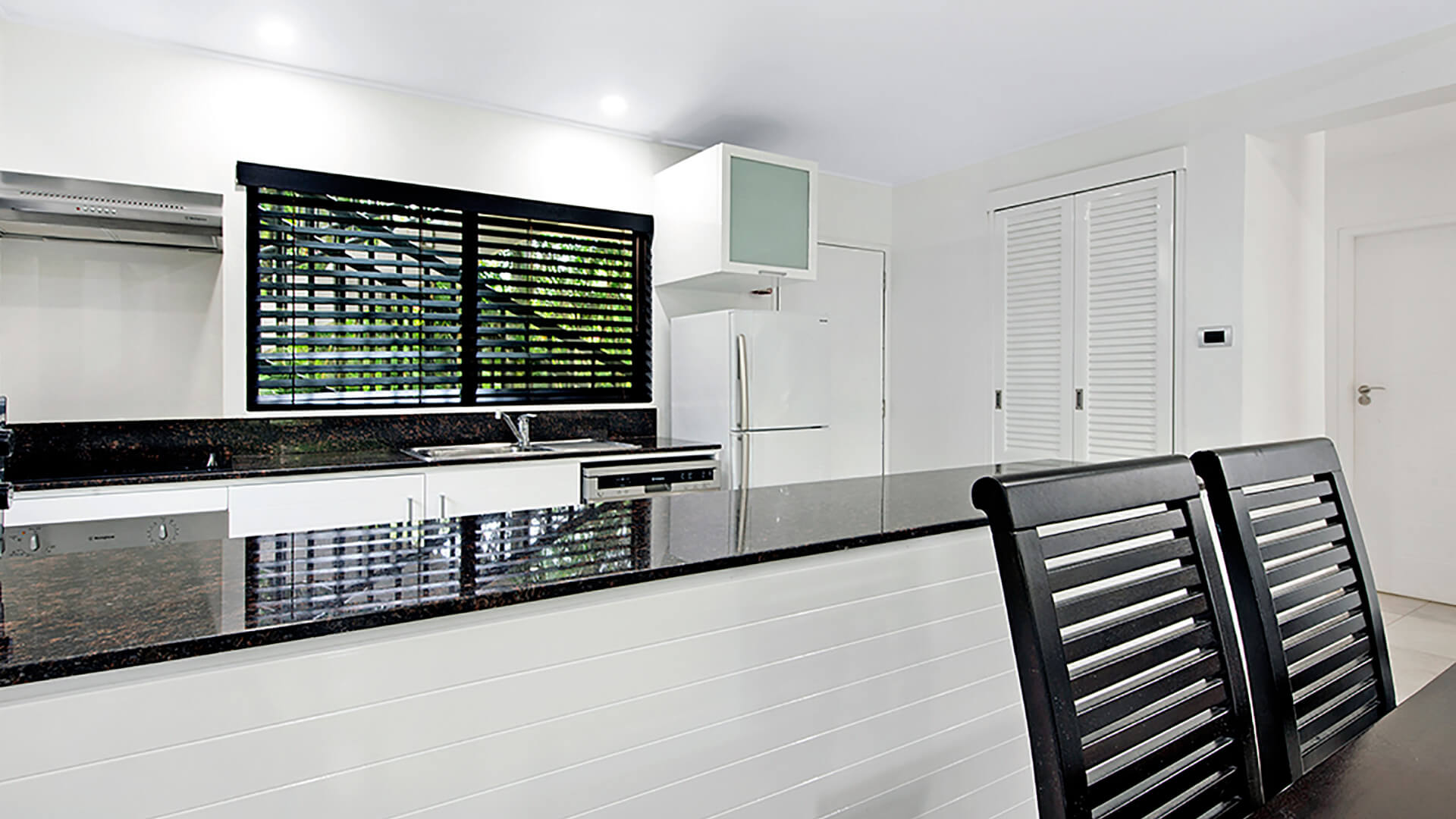 Modern kitchen featuring sleek black granite countertops, stainless steel appliances, and stylish louvered windows for natural light.