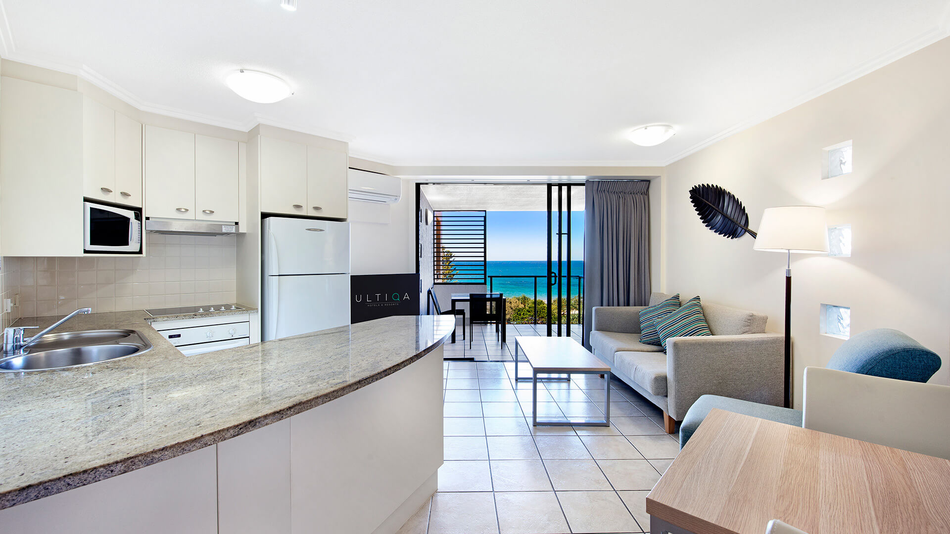 Kitchen and living area with ocean-view balcony in 1 Bedroom Apartment at ULTIQA Shearwater Resort.