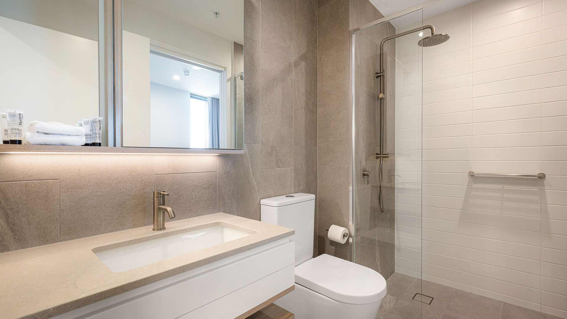 Modern bathroom in a 2 Bedroom Suite at ULTIQA Signature at Broadbeach, featuring a glass-enclosed shower, toilet, and sleek vanity with large mirror.
