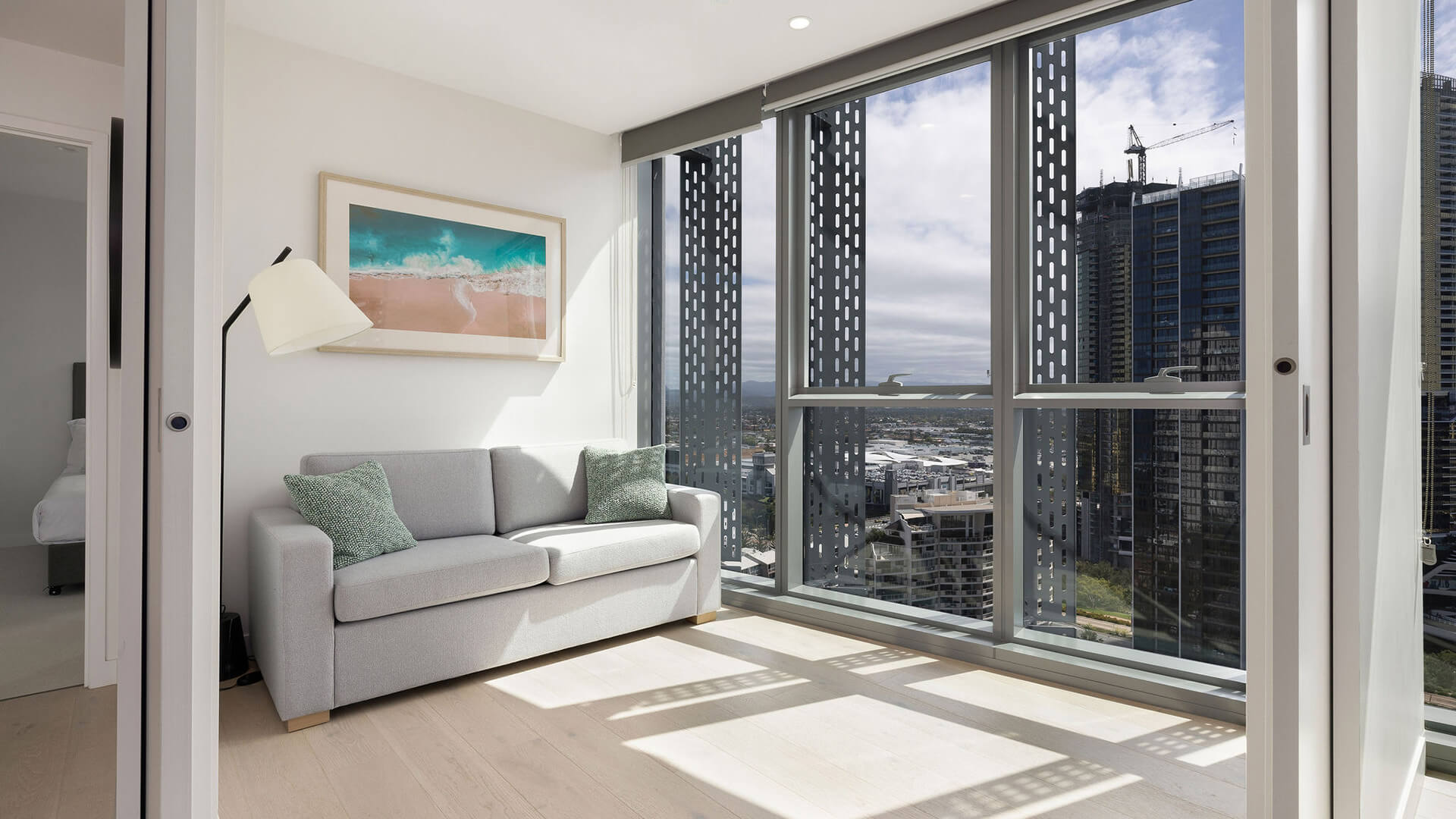 Bright sitting area with sofa, floor lamp, and floor-to-ceiling windows offering city views in the 2 Bedroom Skyhome at ULTIQA Signature at Broadbeach.