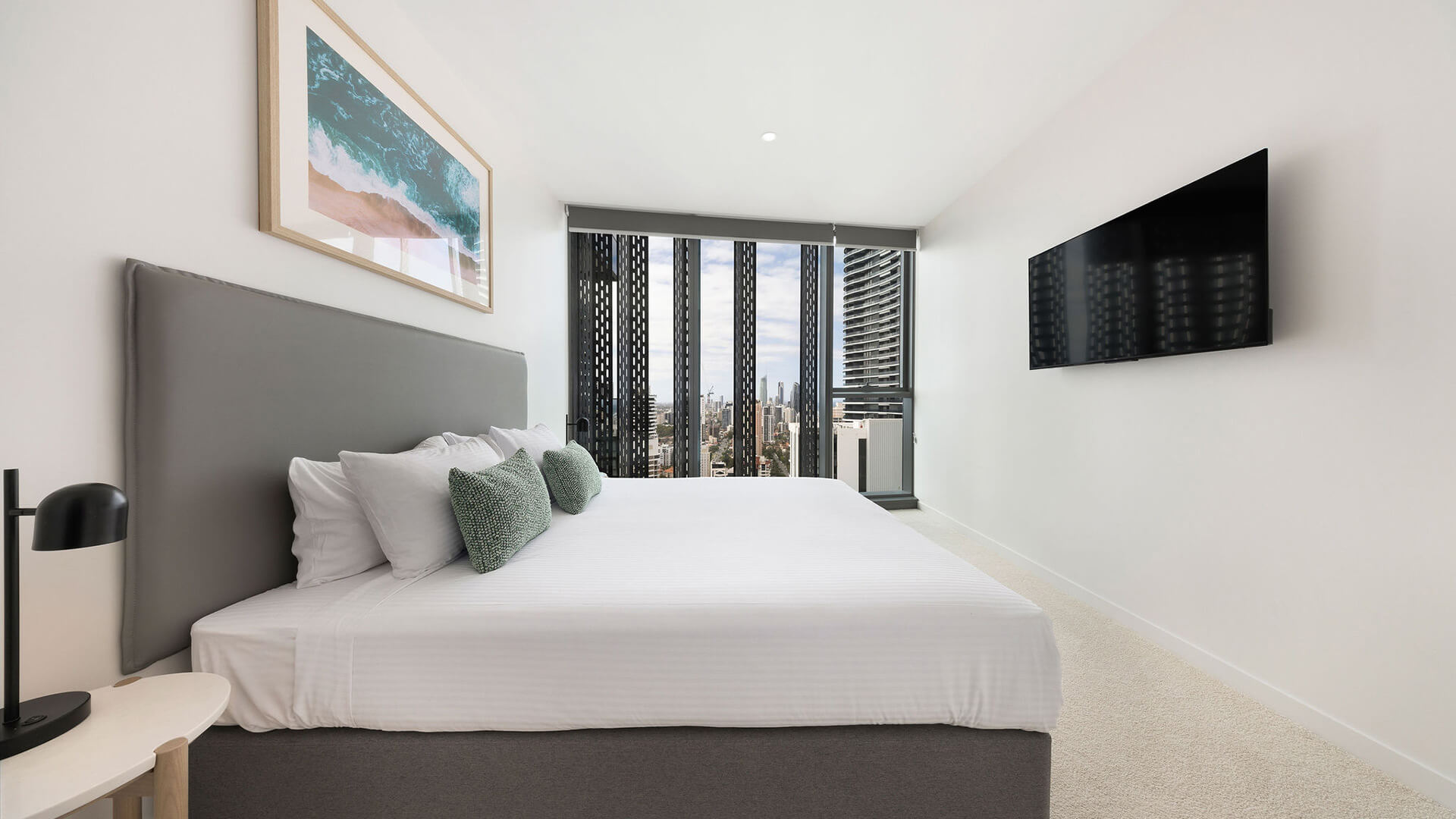 Master bedroom with king bed, wall-mounted TV, and floor-to-ceiling windows showcasing panoramic city views in the 2 Bedroom Skyhome at ULTIQA Signature at Broadbeach.