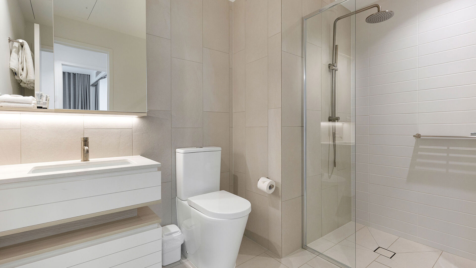 Bathroom in 3 Bedroom Suite at ULTIQA Signature, featuring vanity, toilet, and glass-enclosed shower with neutral-toned tiles.