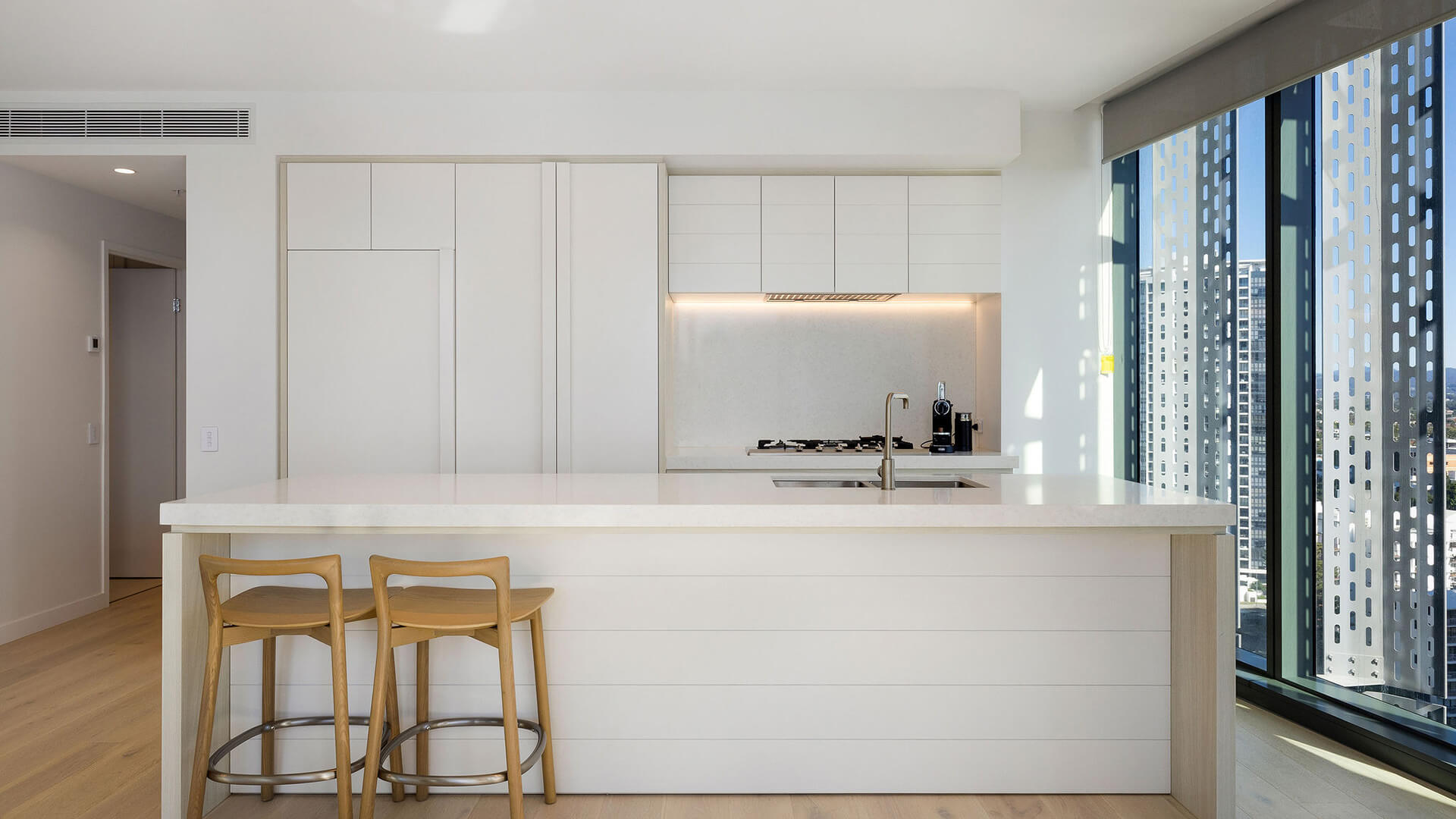 Kitchen in 3 Bedroom Suite at ULTIQA Signature, featuring a large island, built-in appliances, and city views through tall windows.