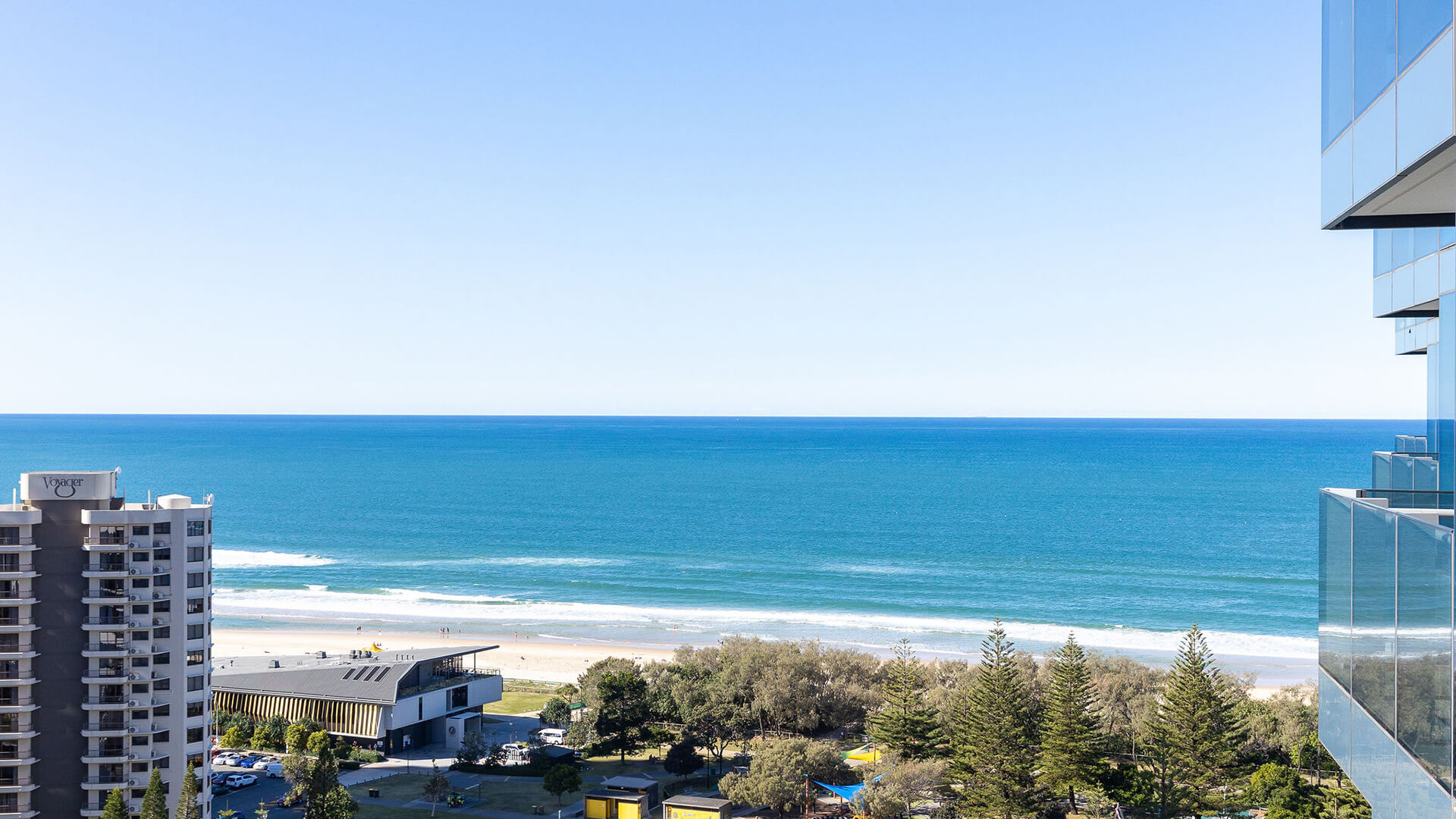 View from 3 Bedroom Suite at ULTIQA Signature, showing coastal cityscape, sandy beach, and blue ocean under a clear sky.