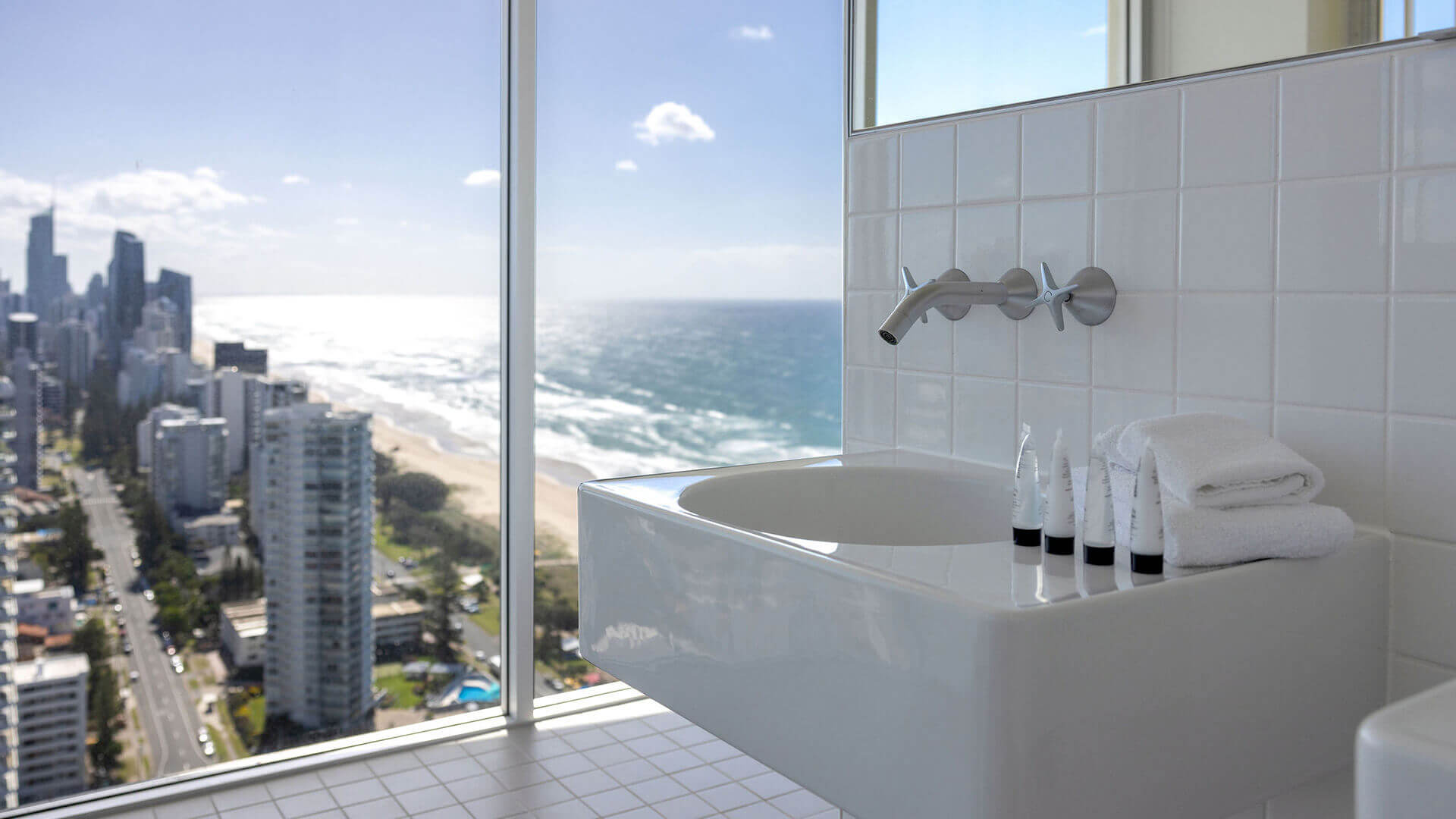 Modern bathroom in ULTIQA Air’s 3 Bedroom Ocean View Suite with sleek white basin, luxury toiletries, and panoramic coastal views through floor-to-ceiling windows.