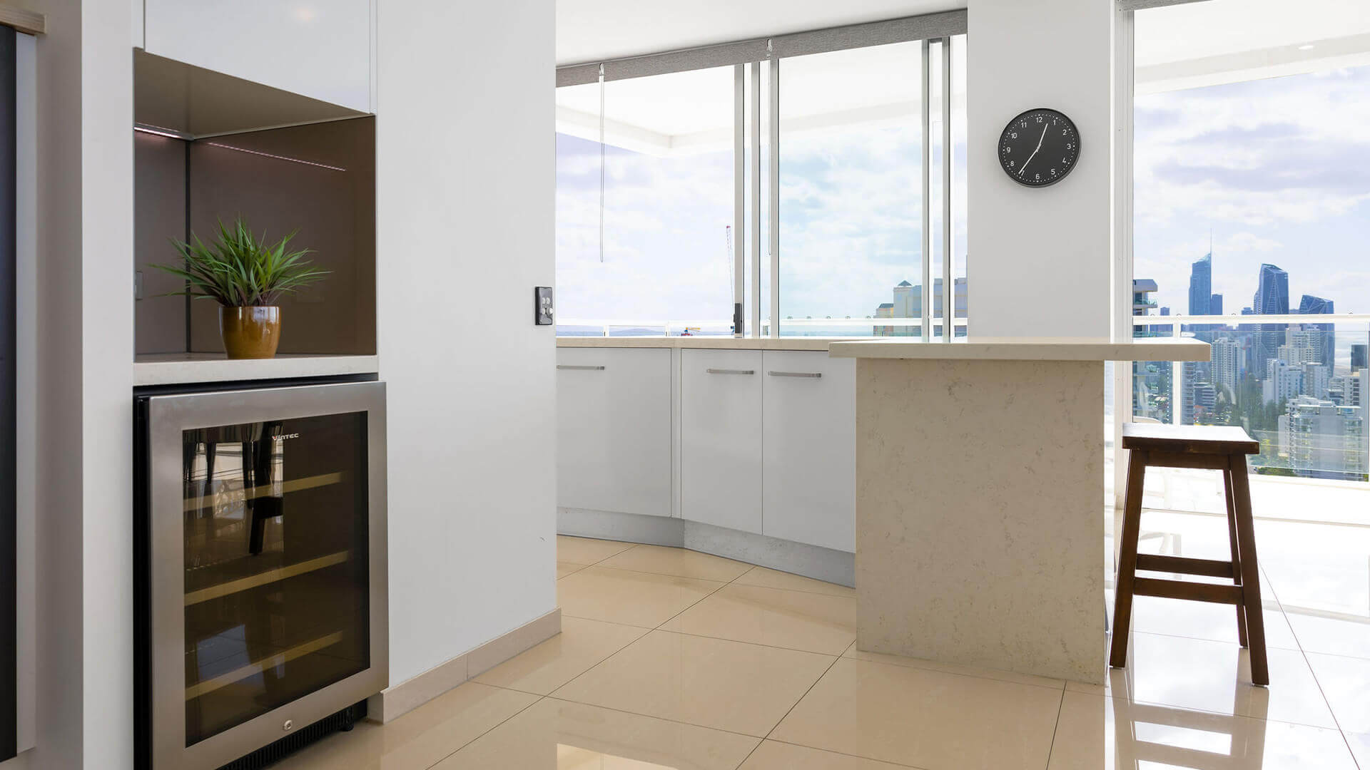 Kitchen with wine cooler, white cabinetry, and city views in ULTIQA Air’s 3 Bedroom Ocean View Suite.