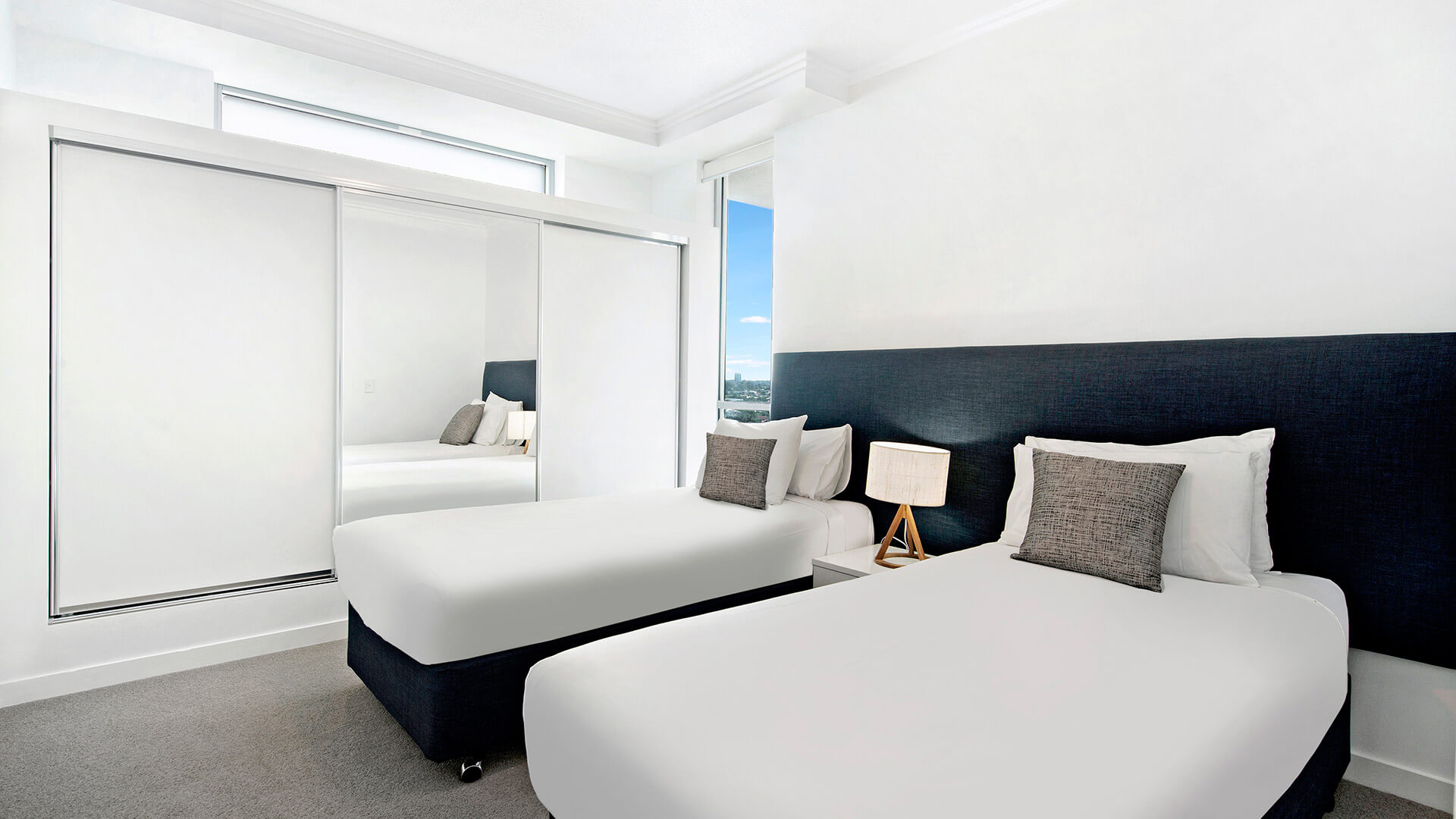 Second bedroom with two single beds, mirrored wardrobe, and city views in the 3 Bedroom Apartment at ULTIQA Freshwater Point Resort.